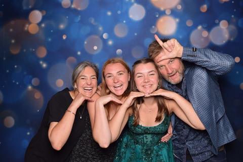 Four people hamming it up in front of a sparkly blue photo booth backdrop