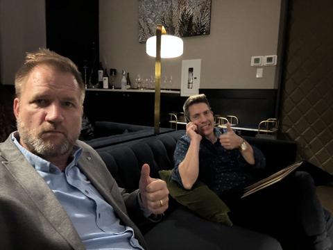 James and a friend on the phone giving a thumbs up in a lounge