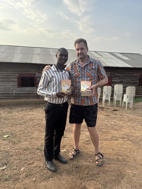 James and a friend each holding a book in front of a wooden barn