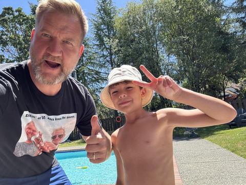 James and a boy in a sun hat giving a peace sign by the pool
