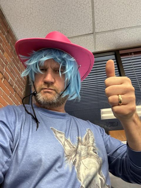 James in a blue wig and pink cowboy hat giving a thumbs up