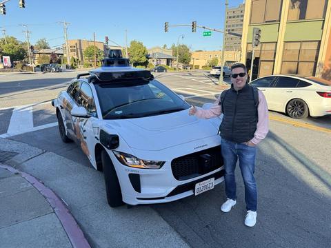 A man standing beside a white Waymo self-driving car at an intersection