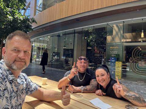 James with two friends at an outdoor table giving thumbs up