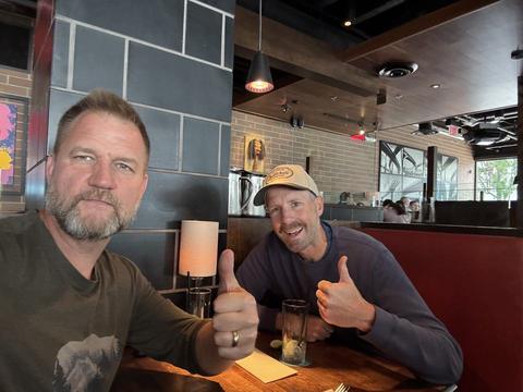 James and a friend in a ball cap at a restaurant booth