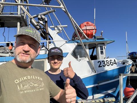 James and a young deckhand giving thumbs up beside a fishing boat