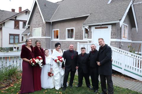 A wedding party in red and black outside a shingled house